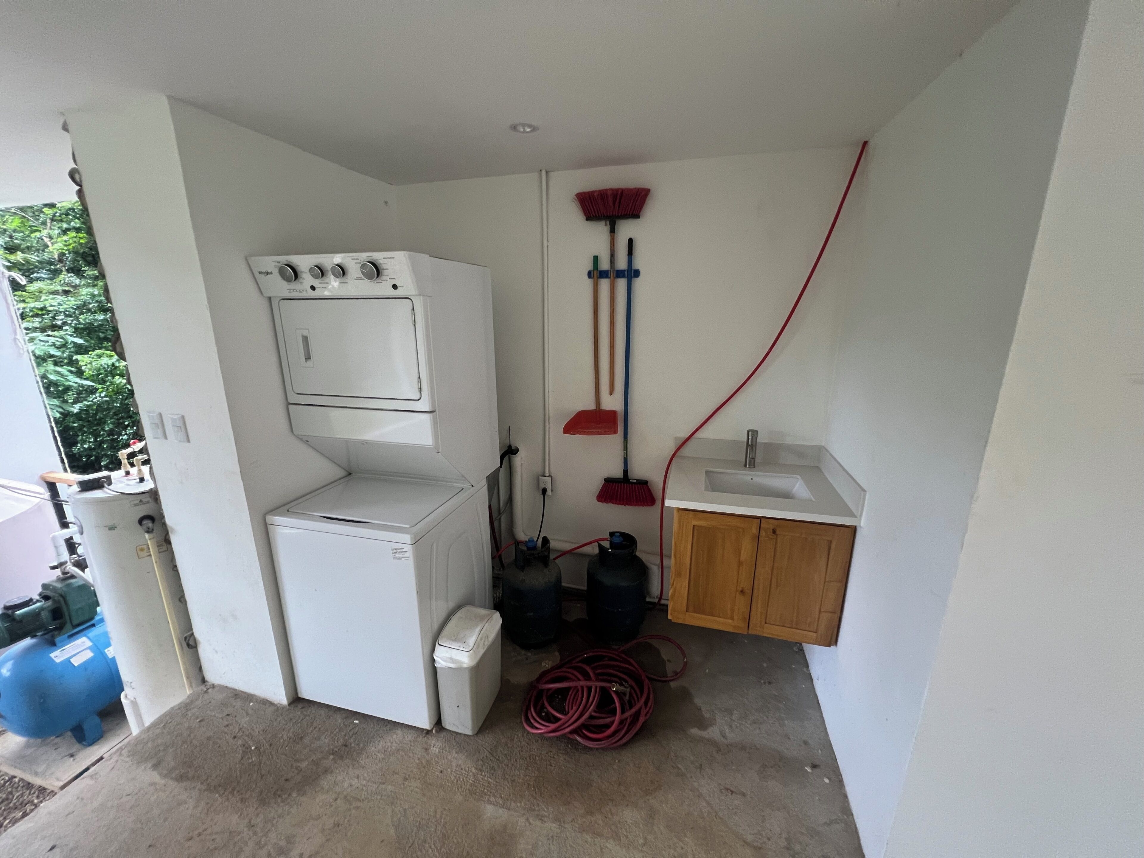 A compact laundry room with a washing machine, a sink, and a broom.