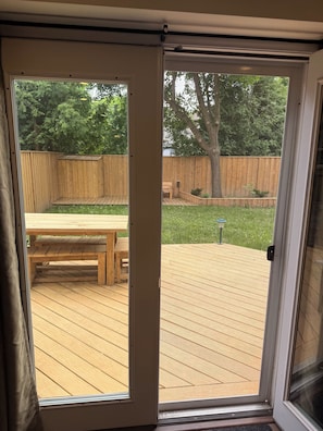 Une porte-fenĂȘtre coulissante donnant sur une terrasse en bois, avec un banc et une table.
