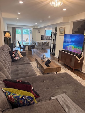 Un salon moderne comprenant un grand canapé, une table basse, un téléviseur à écran plat et un coin repas avec des chaises et une table.