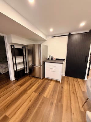 A modern kitchen with a stainless steel refrigerator, white cabinetry, and a wooden floor.
