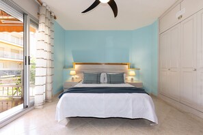 A bedroom with a bed, a ceiling fan, a nightstand, a window with curtains, and a view of a balcony. - Beachfront apartment in Vilafortuny (Cambrils)