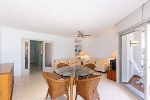 A living room with a glass-top table, wicker chairs, a sofa, and a television. - Beachfront apartment in Vilafortuny (Cambrils)