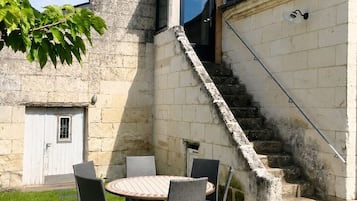 Un edificio de piedra con una terraza de madera, una escalera y una mesa con sillas.