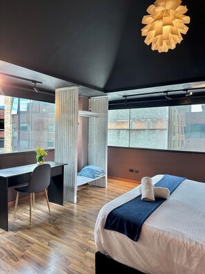 Et moderne hotelværelse med seng, skrivebord, stol, store vinduer og en unik loftlampe.