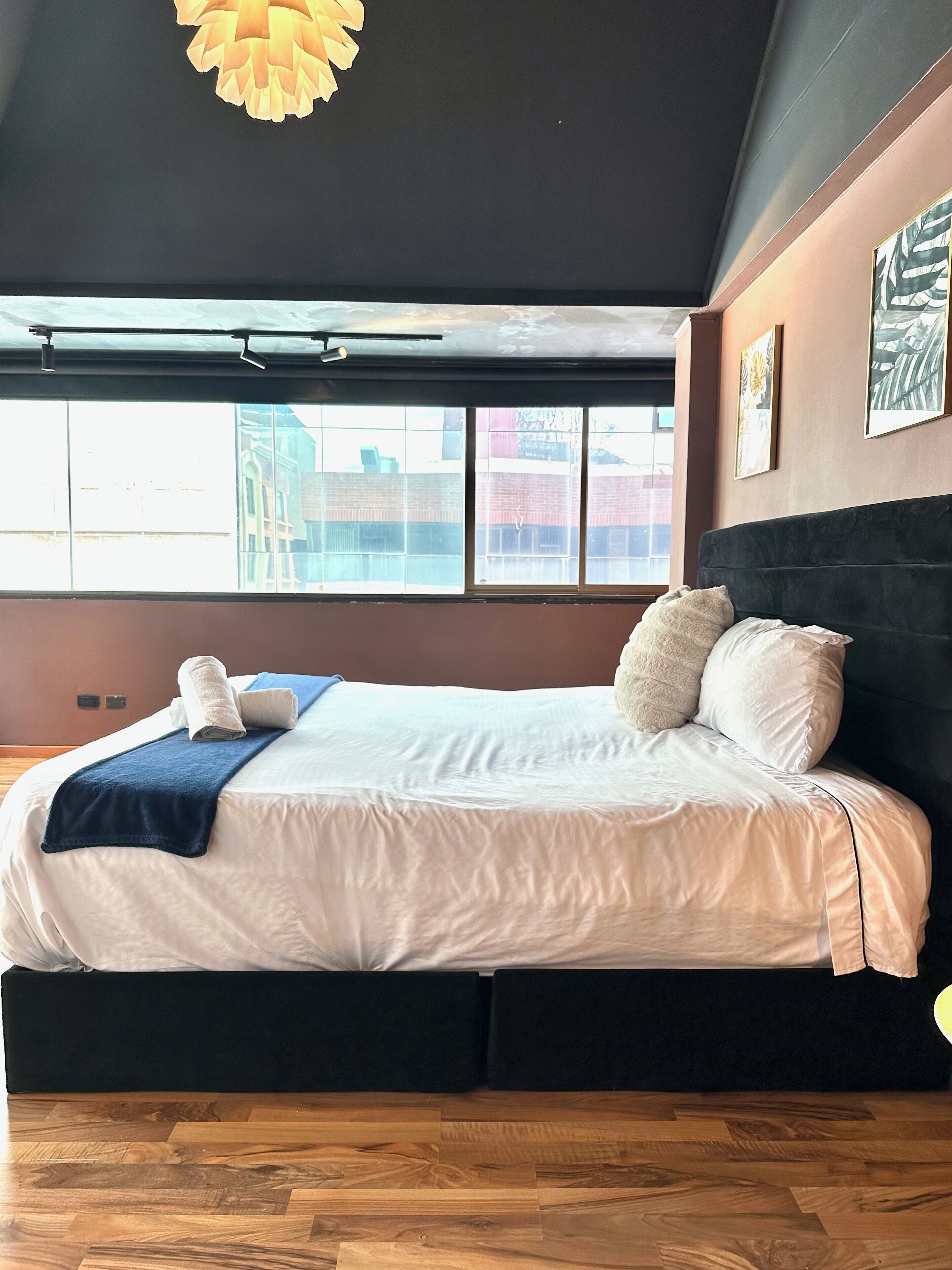 Ein Hotelzimmer mit einem großen Bett, Blick durch ein Fenster und einer Deckenleuchte.