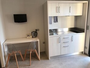 A compact kitchen with a built-in stove, a sink, and a flat-screen TV mounted on the wall. - Les Studios du Centre Buch (La Teste)