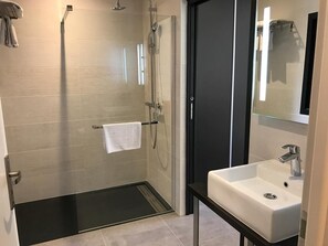 Casa de banho moderna com chuveiro envolto em vidro, pia branca e espelho grande.