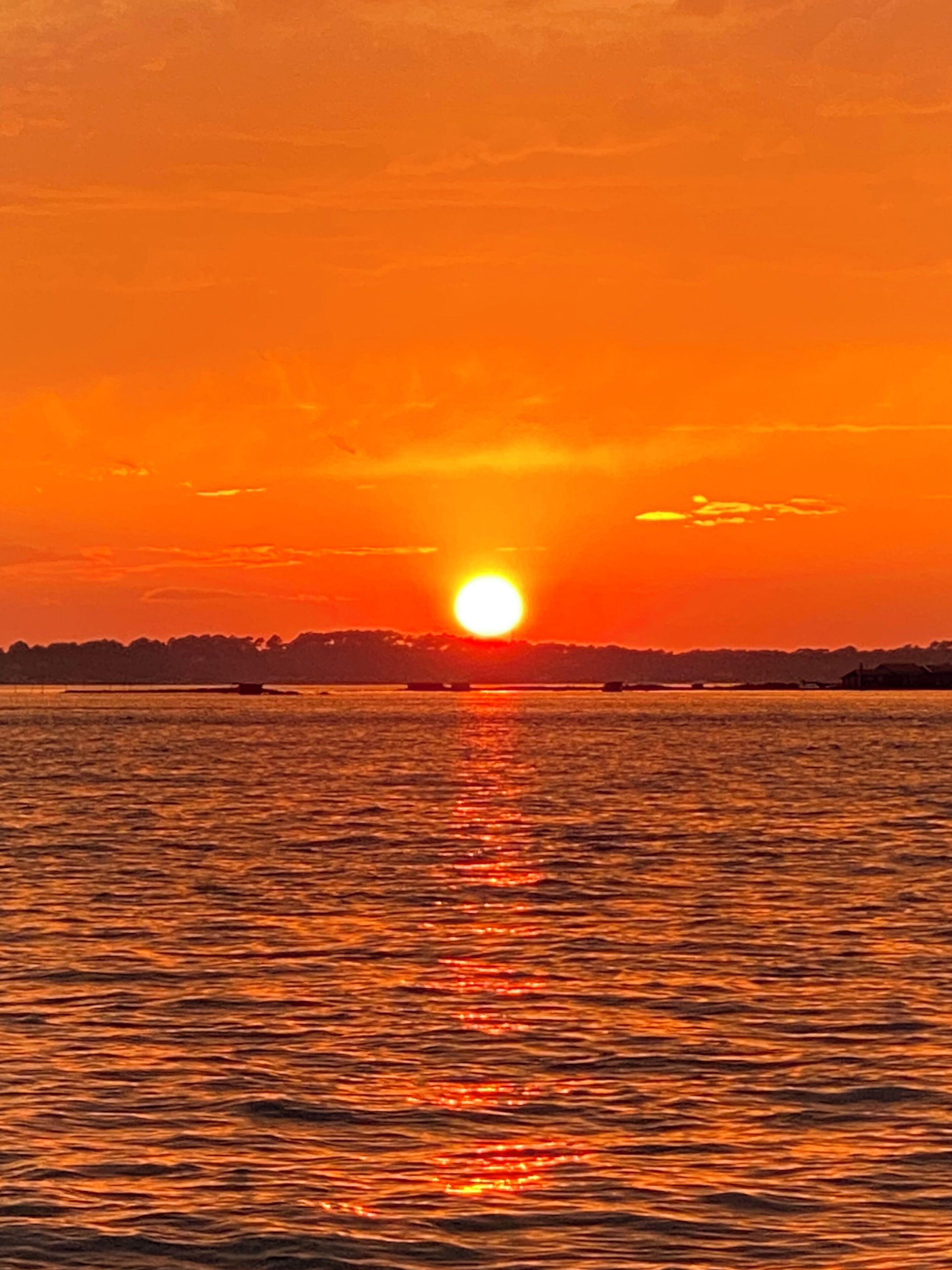 Un atardecer sobre un cuerpo de agua con el silueteado contorno de la costa en la distancia.
