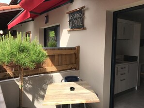 Ein Sitzbereich im Freien mit Tisch und Stühlen, einer hölzernen Bank und einem Schild mit der Aufschrift 'LES STUDIOS DU CENTRE'.