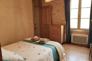 A bedroom with a bed, a dresser, a radiator, and a window with curtains. - In the heart of Monpazier beautiful bright apartment located on the 1st floor (Monpazier)