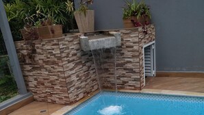 A swimming pool with a waterfall feature, surrounded by stone walls and potted plants. - Mini Club with Biribol (a Brazilian beach volleyball game) (Bertioga)