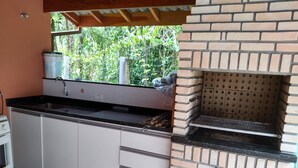 A kitchen with a brick oven, a sink, and a window overlooking greenery. - Mini Club with Biribol (a Brazilian beach volleyball game) (Bertioga)
