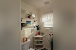 Un baño con inodoro, estantes decorados y una ventana con persianas, además de una planta.