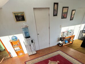 A room with a water dispenser, a coffee machine, a shelf with snacks, a rug, and framed pictures on the wall.
