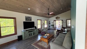 A spacious living room with a wooden ceiling, a large flat-screen TV, a sofa, a coffee table, and a fireplace.