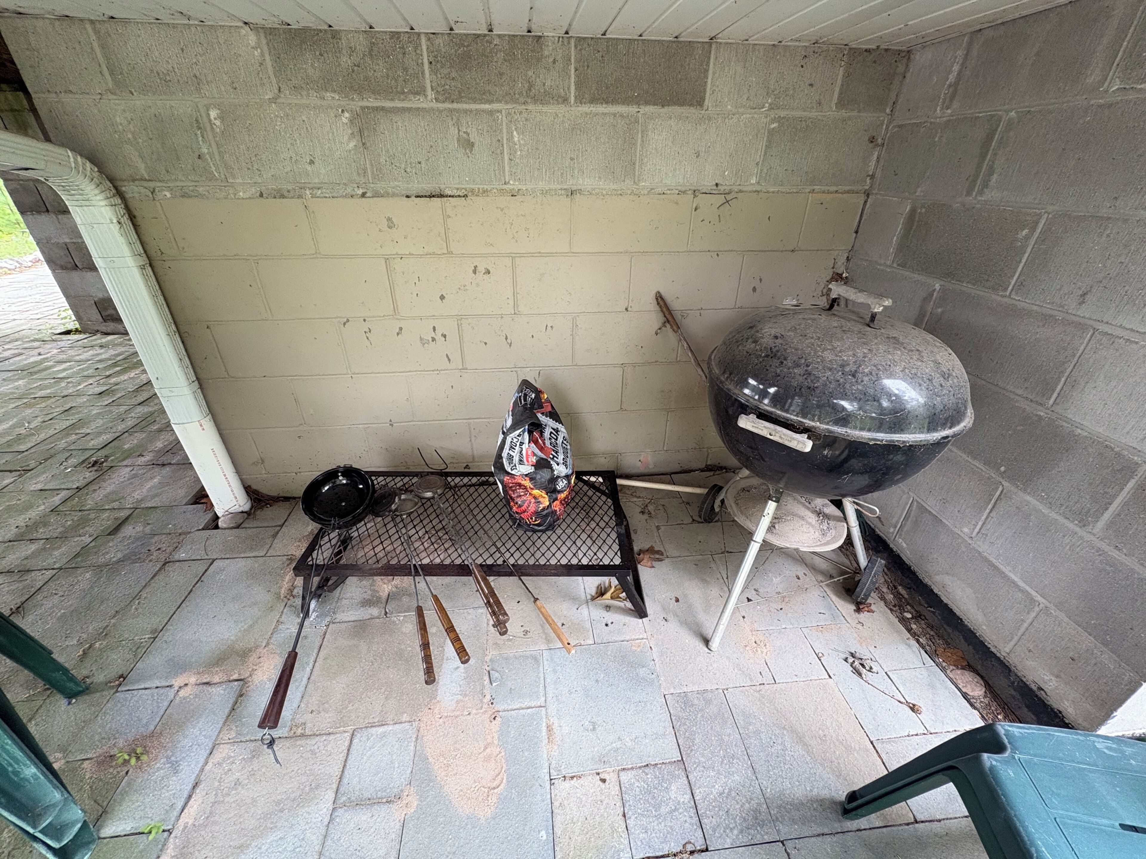 Een barbecue, een metalen grillpan en een zak houtskool op een betegeld terras.