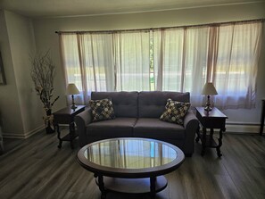 Una sala de estar con un sofá, dos lámparas, una mesa de centro de vidrio y un jarrón con ramas.