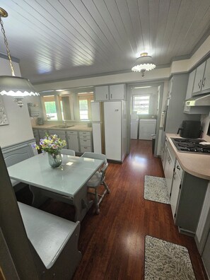 A compact kitchen with wooden flooring, a dining table with chairs, a refrigerator, and a stove.