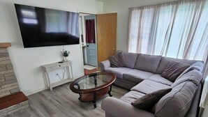 A living room with a grey sofa, a glass coffee table, a television mounted on the wall, and a wooden cabinet. - Snowmobile Sanctuary in the Charming Village of Crivitz (Crivitz)