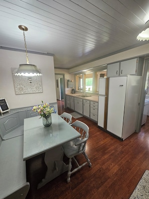 Una cocina con una mesa de comedor, sillas, un refrigerador y una lámpara colgante.