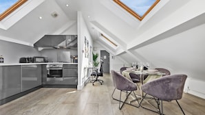 A modern kitchen with a dining area, featuring a skylight, stainless steel appliances, and a dining table with chairs. - Luxe Farringdon Apartments By Stay Smart (London)