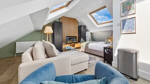 A modern loft bedroom with a sloped ceiling, a sofa, a bed, a TV, and artwork on the walls. - Luxe Farringdon Apartments By Stay Smart (London)