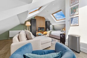 Ein modernes Schlafzimmer im Loft-Stil mit schrägverdeckter Decke, einer Couch, einem Bett, einem Fernseher und Kunstwerken an den Wänden.
