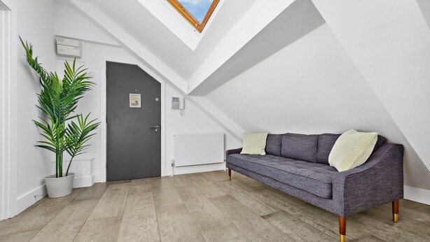 A modern loft bedroom with a skylight, a grey sofa, and a potted plant. - Luxe Farringdon Apartments By Stay Smart (London)