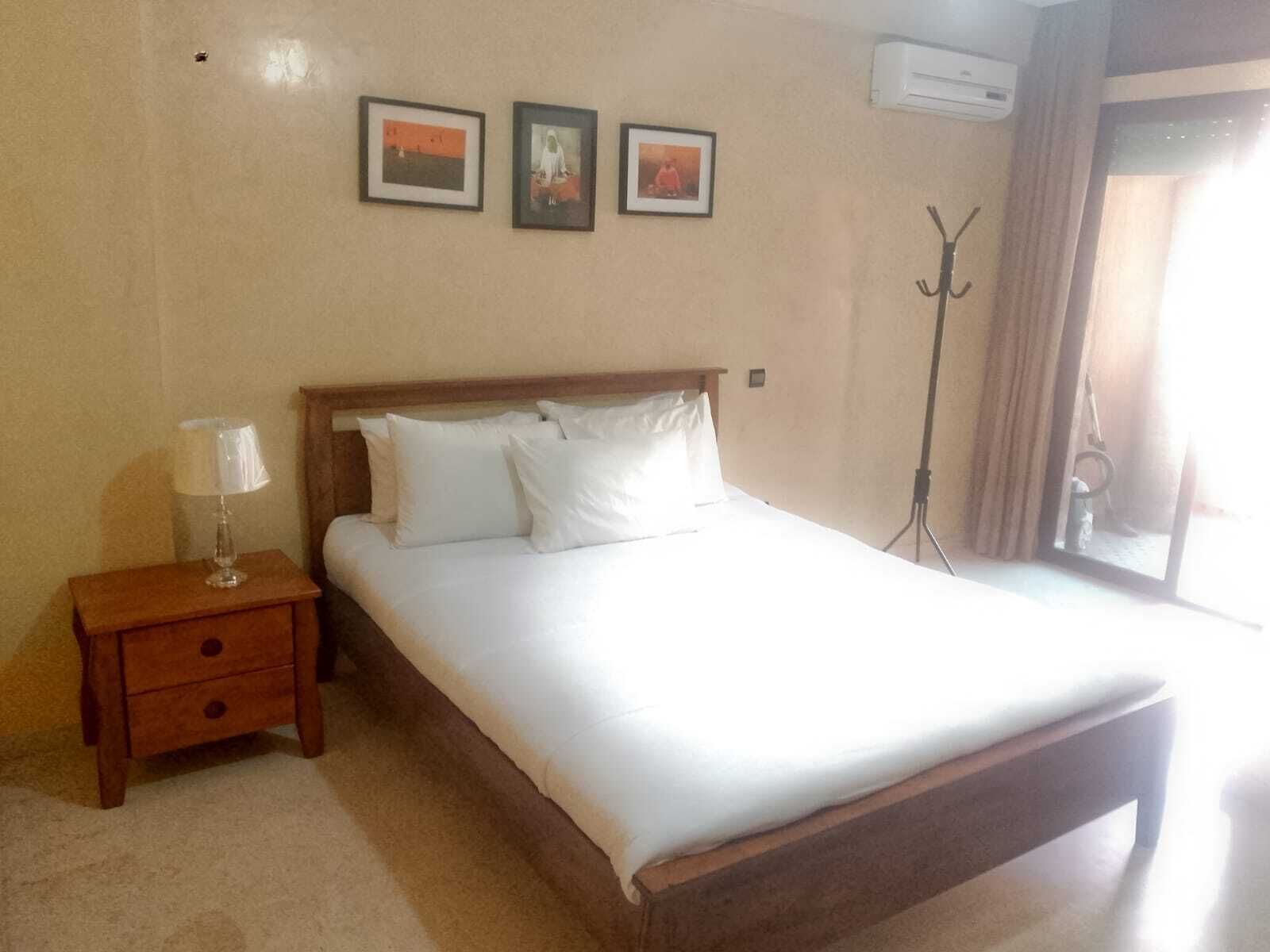 A hotel room with a bed, a nightstand, a lamp, and three framed pictures on the wall.