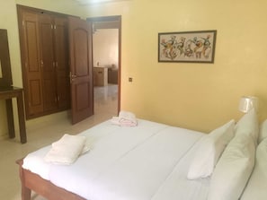 Un dormitorio con una cama, un armario de madera, un cuadro en la pared y una puerta abierta que da a otra habitación.