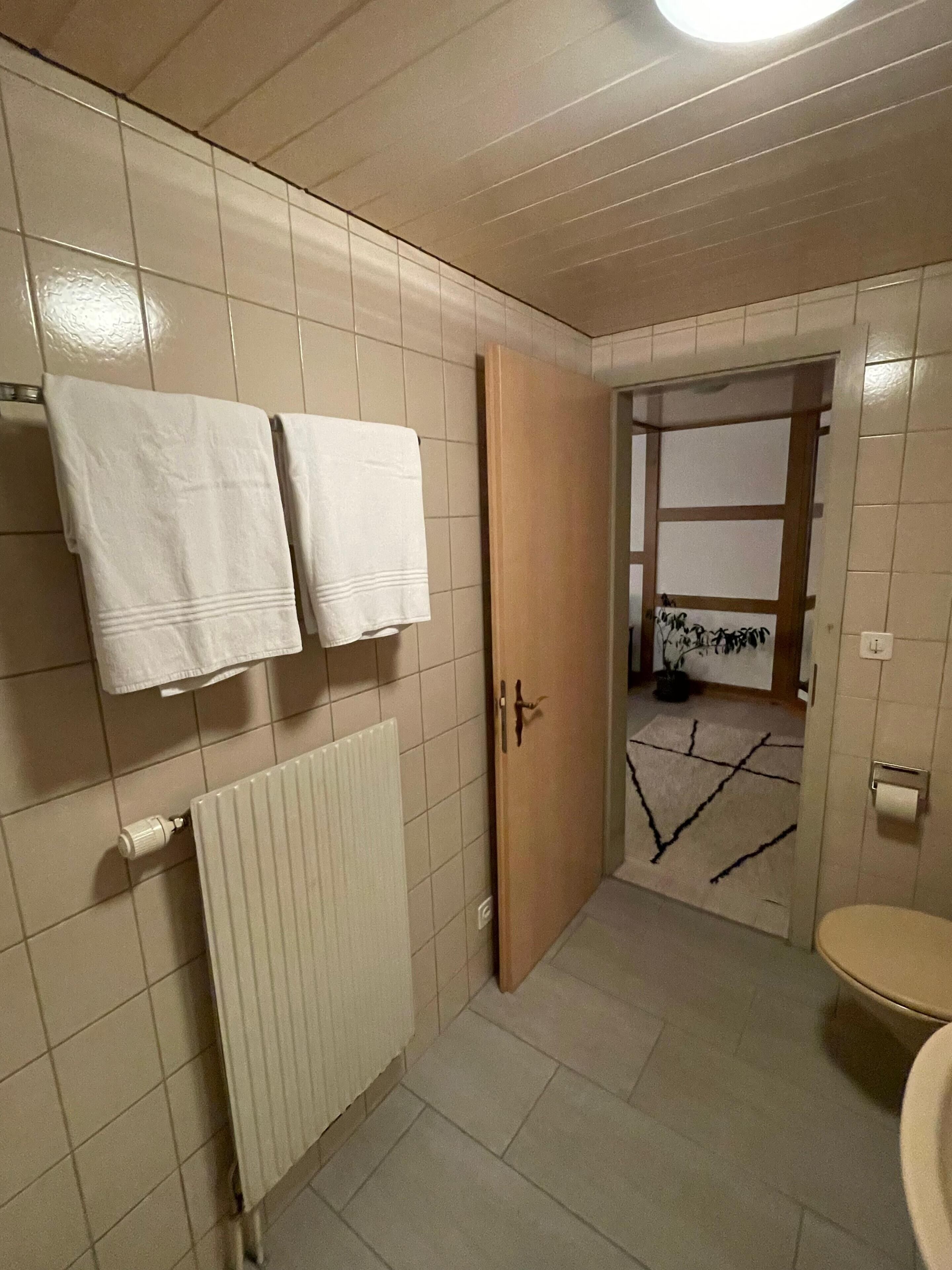 Un bagno con il water, un termosifone e due asciugamani appesi al muro.