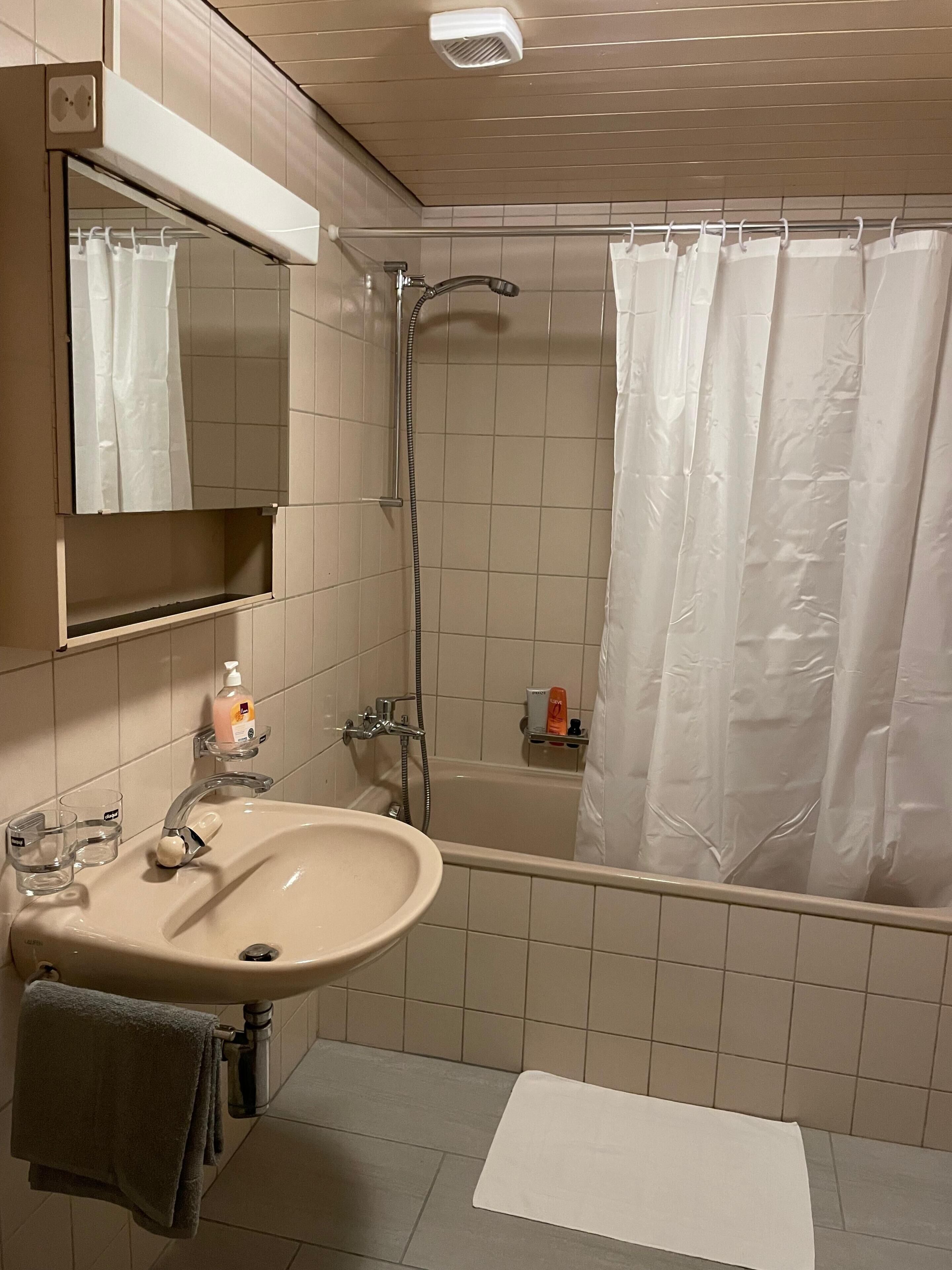 A bathroom with a sink, mirror, shower, and towel rack.