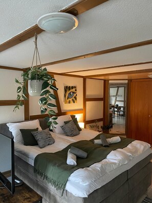 Une chambre à coucher avec un lit, des oreillers, une plante suspendue, un tableau et un plafond en bois.