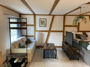 Ein modernes Wohnzimmer mit Sofa, Couchtisch, Fernseher, einer hängenden Pflanze und einem Fenster mit Vorhängen.