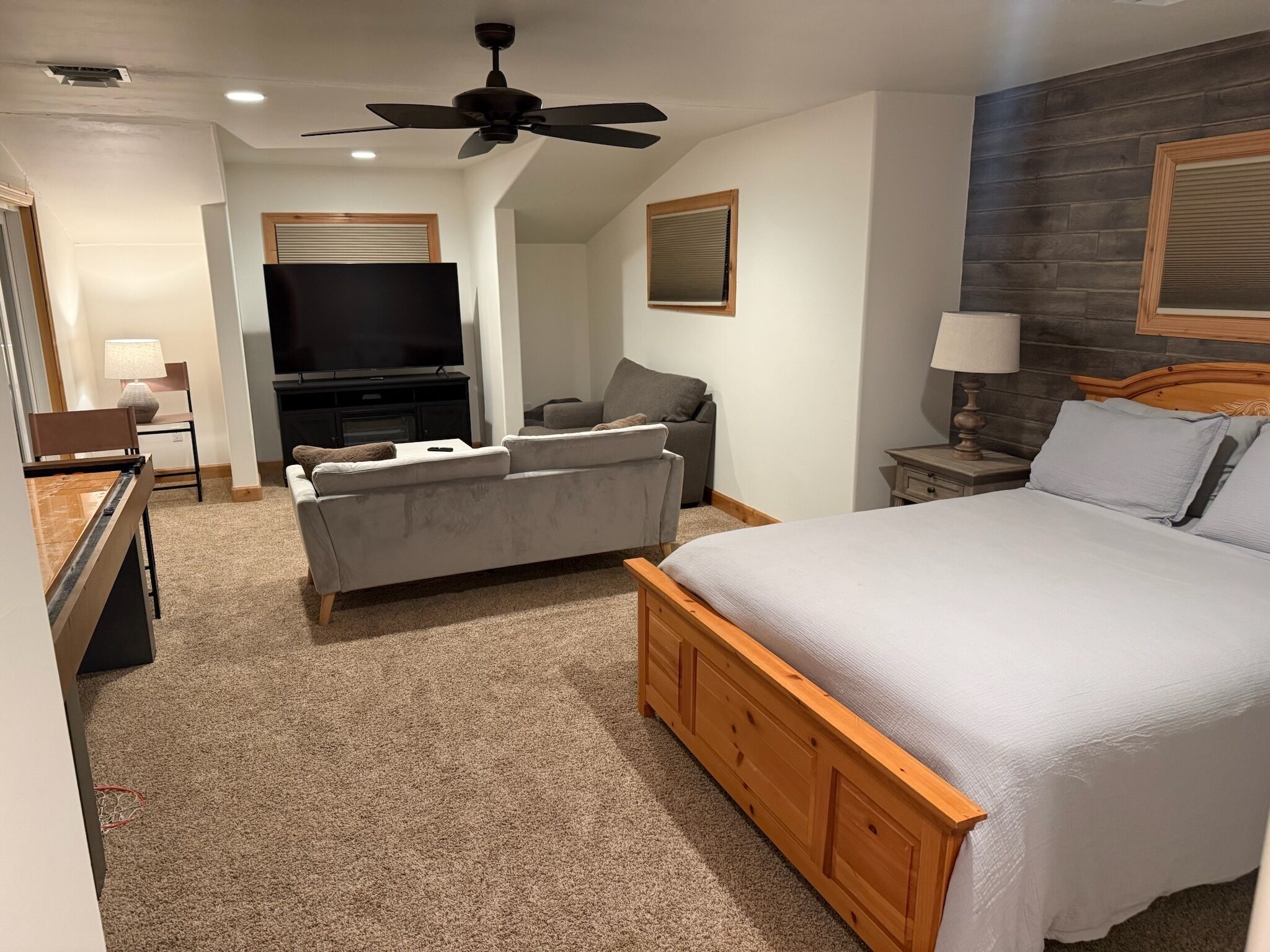 A hotel room with a bed, a sofa, a TV, a ceiling fan, and a wooden headboard.