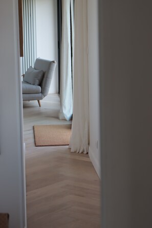 A modern interior with a wooden floor, a grey sofa with cushions, and a white curtain. - Family home in the countryside, 25 km from Rouen (Auzouville-sur-Ry)