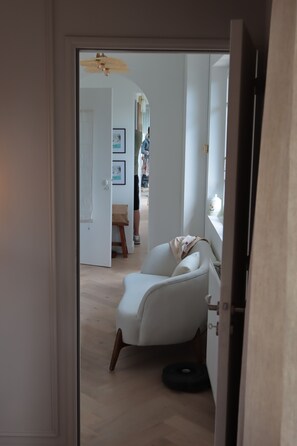 Une porte qui mène à une pièce où se trouvent une chaise blanche, une petite table et une étagère fixée au mur.