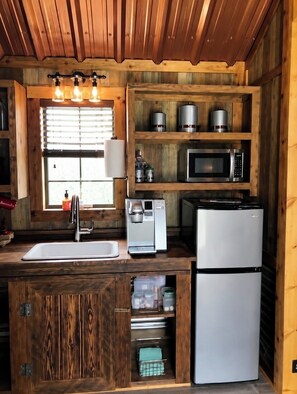A kitchen with wooden walls, a sink, a coffee maker, a microwave, and a refrigerator.