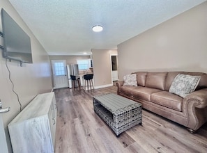 A living room with a brown leather sofa, a coffee table, and a TV mounted on the wall.