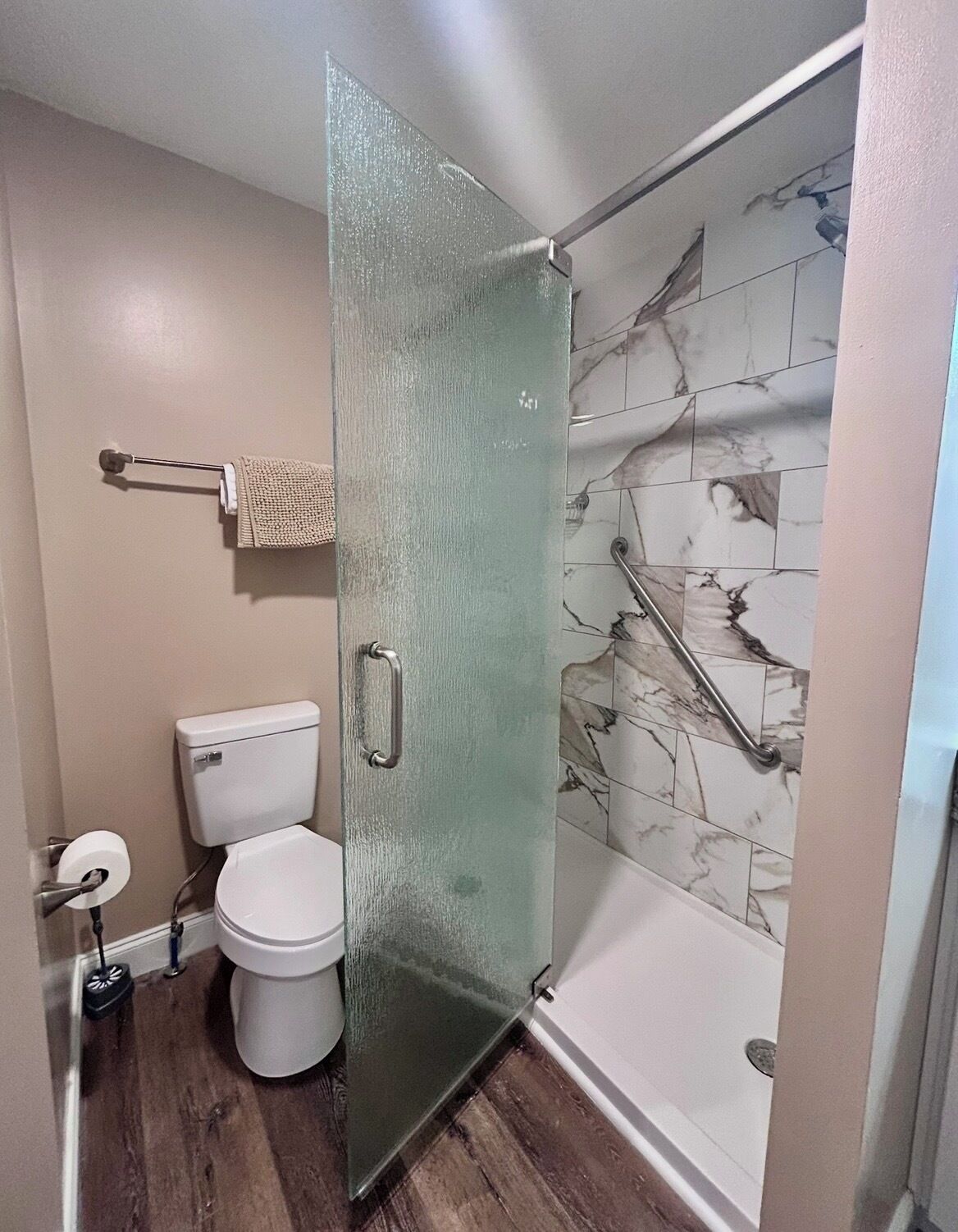 A bathroom with a glass shower door, a toilet, and marble-patterned tiles.