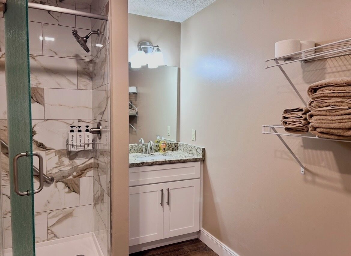 A bathroom with a glass shower enclosure, white cabinets, a sink with a marble countertop, and a towel rack with folded towels.