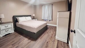 A bedroom with a bed, nightstands, a dresser, and a door. - In-Town Gem • Huge Yard • Near Golf, Food & attractions (Crossville)