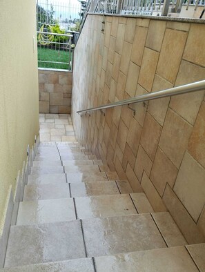 Eine Treppe mit Steinstufen und einem Metallgeländer, die zu einem umzäunten Bereich mit Blick auf Grünflächen führt.