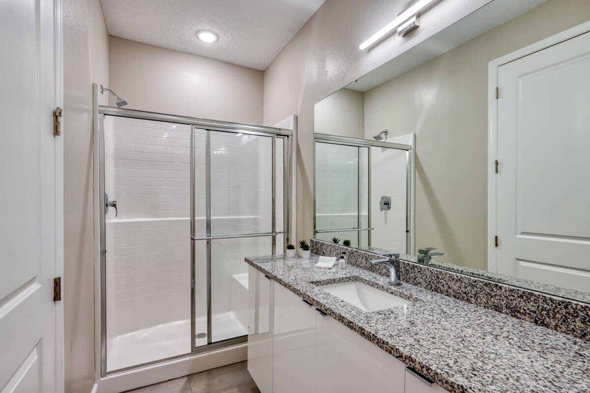 A bathroom with a glass shower enclosure, a granite countertop sink, and a large mirror.
