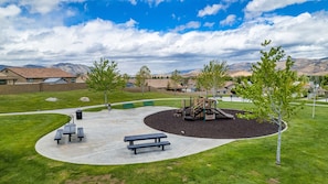 A playground with benches and a slide, surrounded by grass and trees.
