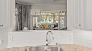 A kitchen with a window view of a patio area, a stainless steel sink, and white tiled walls. - Callawassie Island Beautiful 3BR/3BA Retreat Free Golf, Riverfront Pools (Okatie)