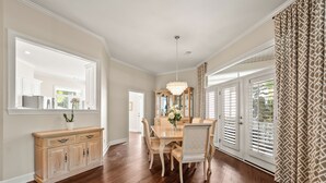 A dining room with a wooden table, chairs, a chandelier, and a large window with shutters. - Callawassie Island Beautiful 3BR/3BA Retreat Free Golf, Riverfront Pools (Okatie)