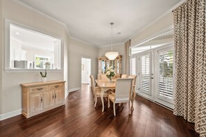 A dining room with a wooden table, chairs, a chandelier, and a large window with shutters. - Beautiful Renovated 3BR/3BA Retreat Free Golf, Riverfront Pools & Resort Living (Okatie)