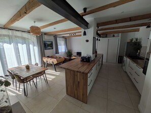 Une cuisine moderne avec des poutres en bois, un îlot central et un coin repas comprenant une table et des chaises.