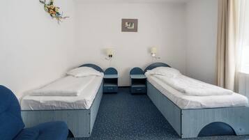 A hotel room with two single beds, a small desk, a chair, a wall-mounted lamp, and a framed picture.